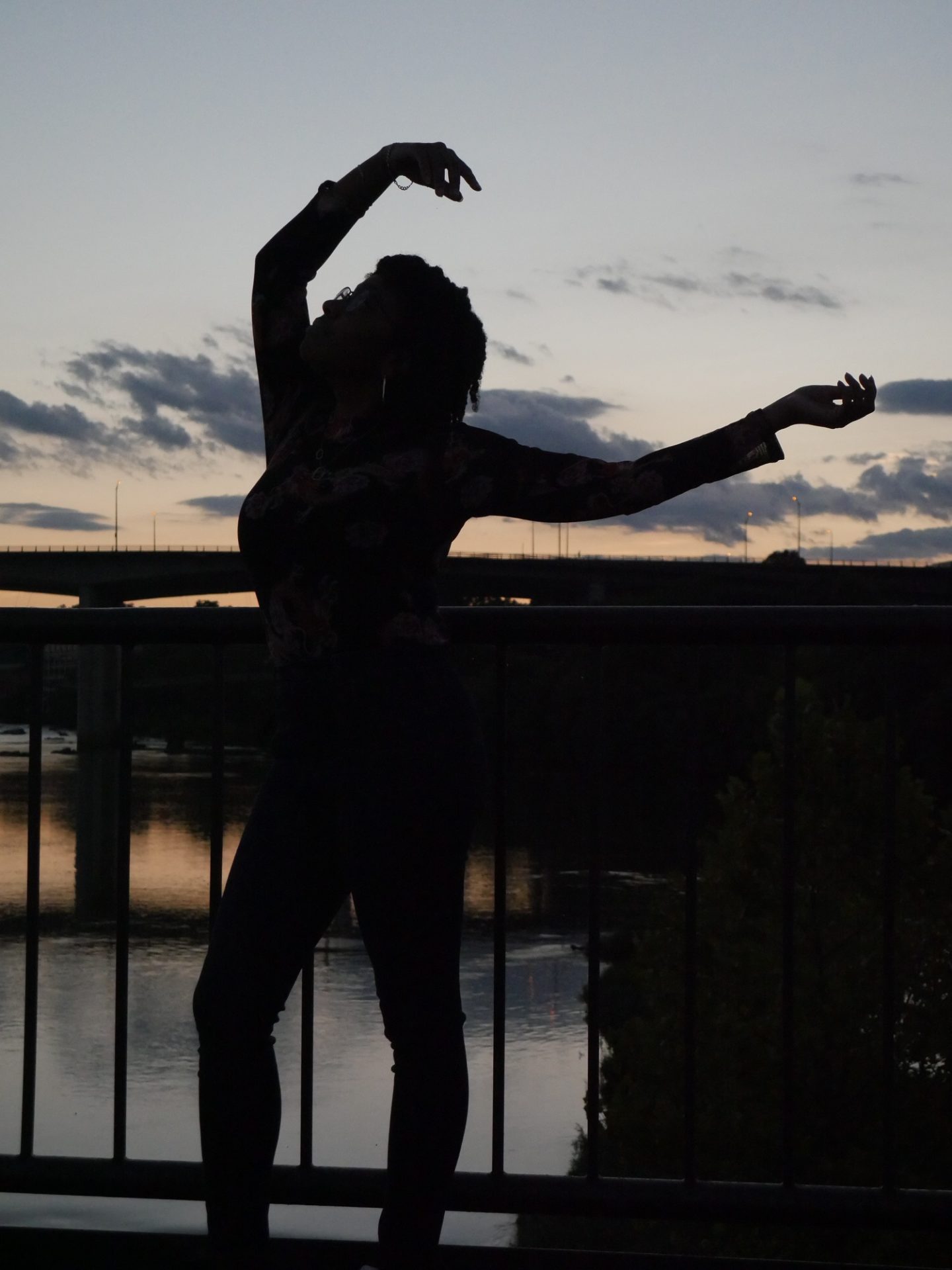 person posing in front of a sunset with a bridge in the background